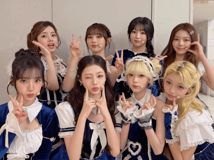 A group of eight young women striking playful poses while wearing matching navy blue and white outfits, showcasing a cheerful atmosphere.