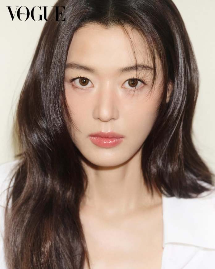 Close-up portrait of Jun Ji-hyun with long dark hair and natural makeup, looking directly at the camera with a neutral expression, against a soft beige background. The top left corner features the logo of Vogue Korea.