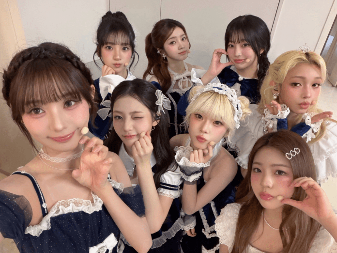 A group selfie of eight young women posing playfully in matching outfits, featuring a mix of cute and stylish elements, set in a bright indoor environment.