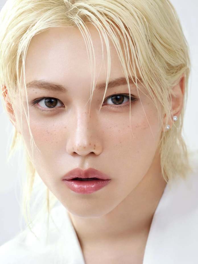 Close-up portrait of Felix with blonde hair and brown eyes, featuring a natural look with freckles and subtle makeup.