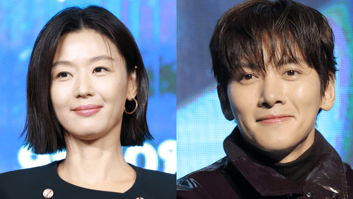 A close-up shot ofJun Ji-hyun and Ji Chang-wook , Jun Ji-hyun  with straight black hair and hoop earrings, and Ji Chang-wook with tousled hair, both smiling against a blue background.