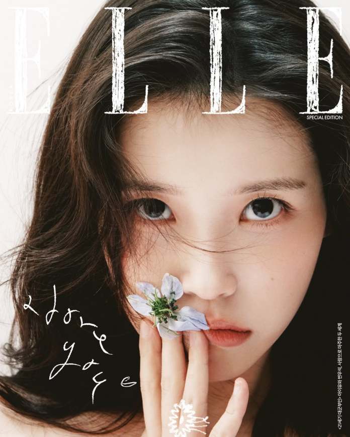 Close-up of IU's face with long dark hair, holding a small blue flower near her lips. The image features the word 'ELLE' at the top and includes handwritten text that says 'I love you.'