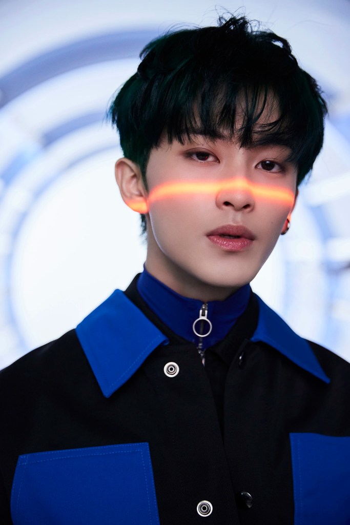 Mark Lee with dark hair and a stylish outfit featuring blue accents, standing against a circular abstract background with a subtle red light stripe across their face.