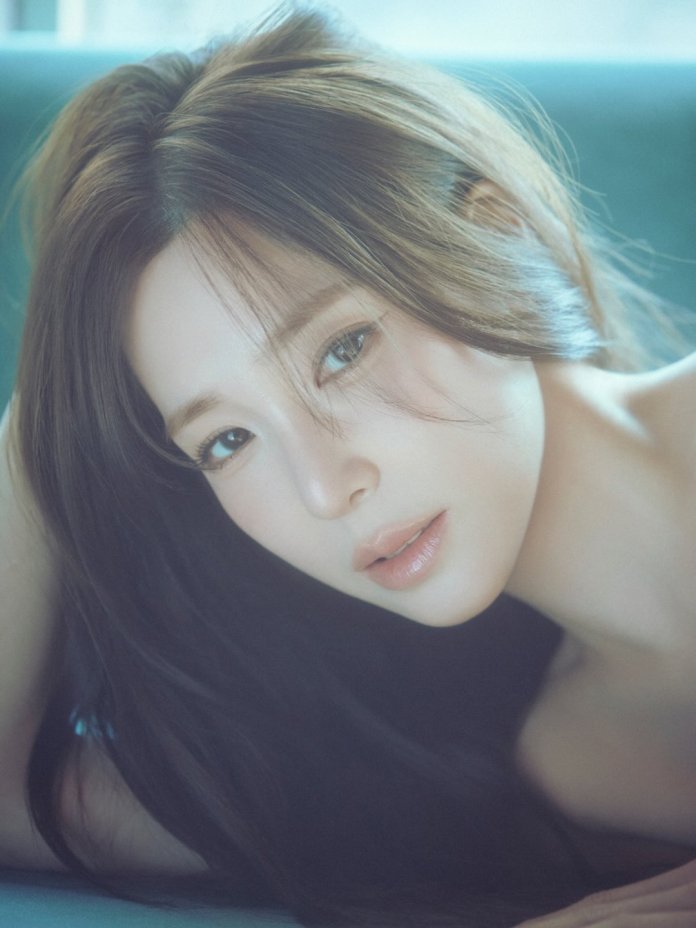 A close-up portrait of Tiffany Young with long, flowing hair, gazing softly at the camera with a serene expression.
