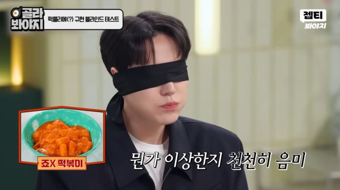 Kyuhyun with a blindfold is tasting food, with a bowl of tteokbokki displayed next to them.
