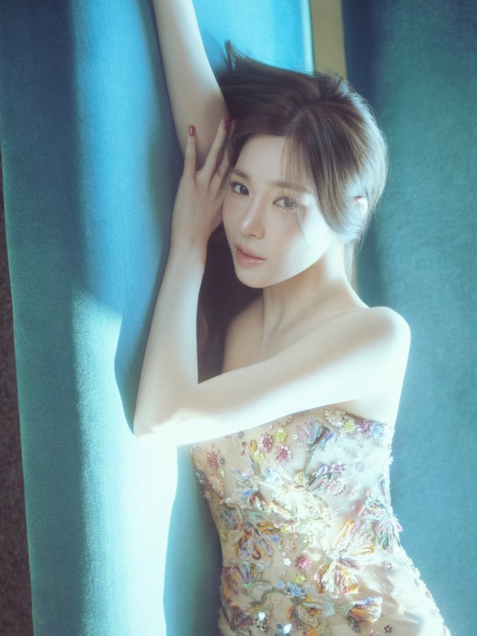 Tiffany Young with long hair poses gracefully against a blue backdrop, wearing a floral embroidered gown.