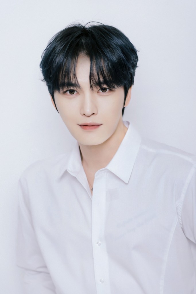 Kim Jae-joong with dark hair styled in soft waves, wearing a white button-up shirt, looking directly at the camera against a plain white background.