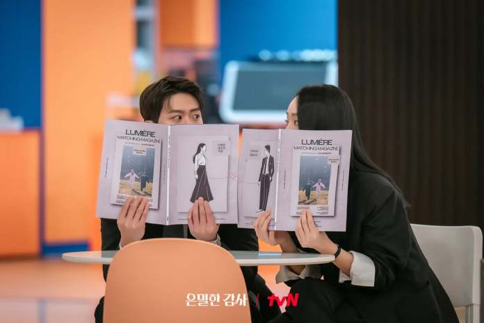 Shin Hye Sun and Gong Myung sitting at a table, both holding matching magazines in front of their faces, with colorful backgrounds.