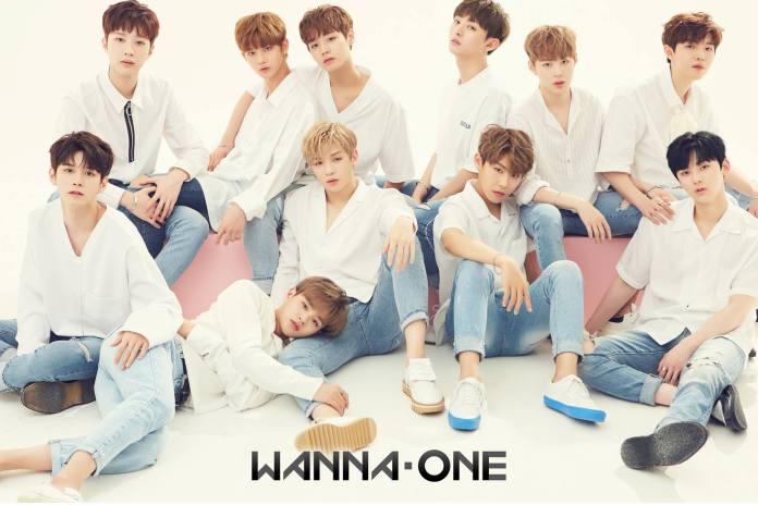 Wanna One posing together, dressed in white shirts and blue jeans, with a light background. The group is sitting and standing in various poses, showcasing a friendly and stylish appearance. The name 'Wanna One' is displayed at the bottom.