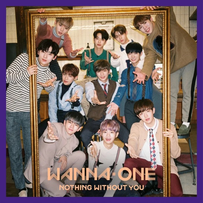 A group photo of the K-pop group Wanna One, featuring all 11 members playfully posing with their arms outstretched in front of a large ornate frame, set in a cozy indoor environment.