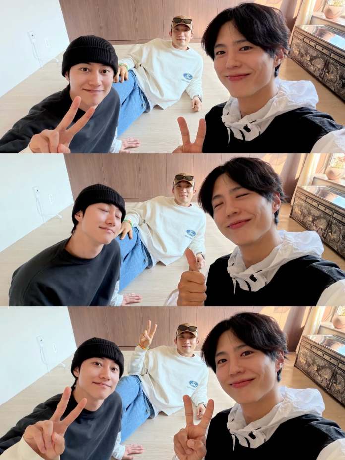 A group selfie featuringPark Bo-gum, Lee Sang-yi, and Kwak Dong-yeon in casual attire, sitting on the floor and making playful hand gestures like peace signs and thumbs up. They are smiling in a bright indoor setting with natural light.