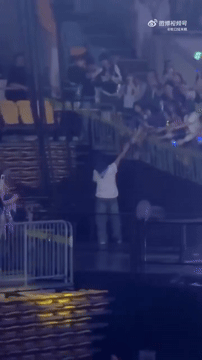 Ryeowook in a white shirt stands on a raised platform, reaching out to a crowd while others wave and cheer in response.