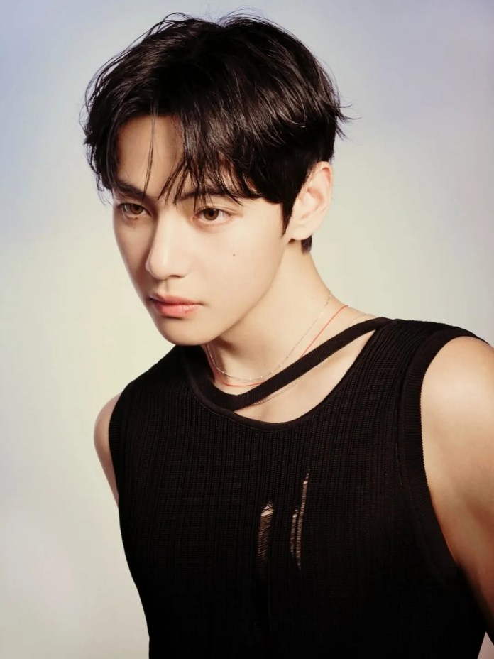 V with dark hair styled casually, wearing a sleeveless black top with a cutout detail, looking thoughtfully to the side against a soft gradient background.
