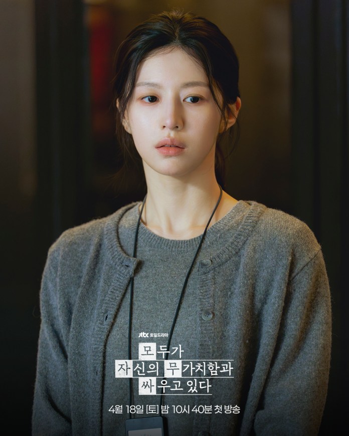 Go Youn-jung with long dark hair wearing a gray cardigan, looking contemplative against a blurred background.