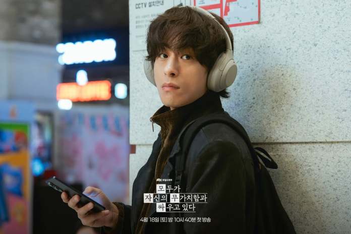 Koo Kyo-hwan wearing headphones, looking thoughtfully at their phone while leaning against a wall in a busy urban setting.