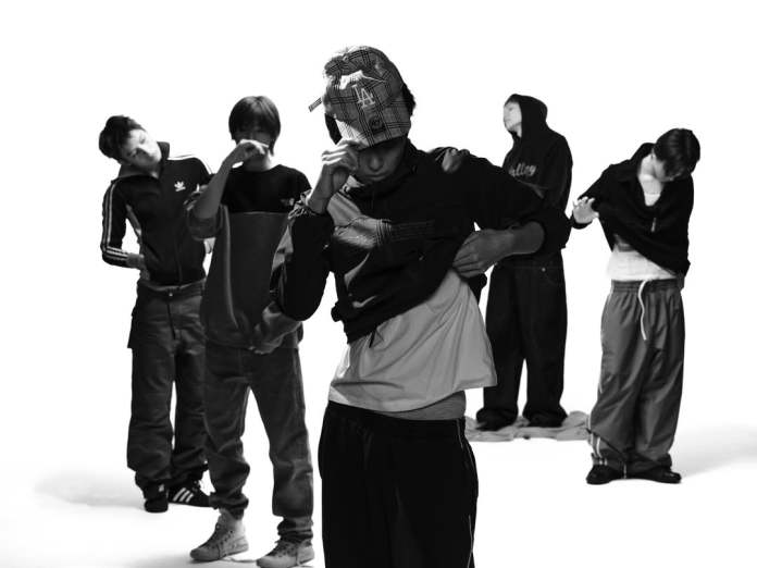 CORTIS members in casual wear, including hoodies and sportswear, are in a studio setting with a white background, with one man changing his shirt in the foreground.