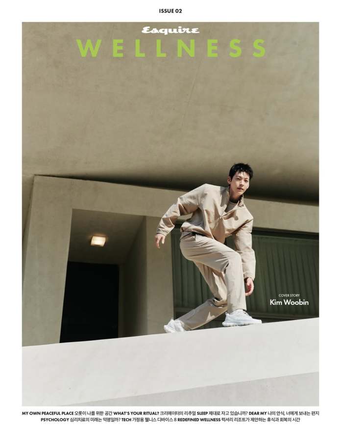 Kim Woo-bin in a beige outfit poses dynamically on a concrete structure for the cover of Esquire's wellness issue, with bold text highlighting 'WELLNESS' and his name, Kim Woobin.