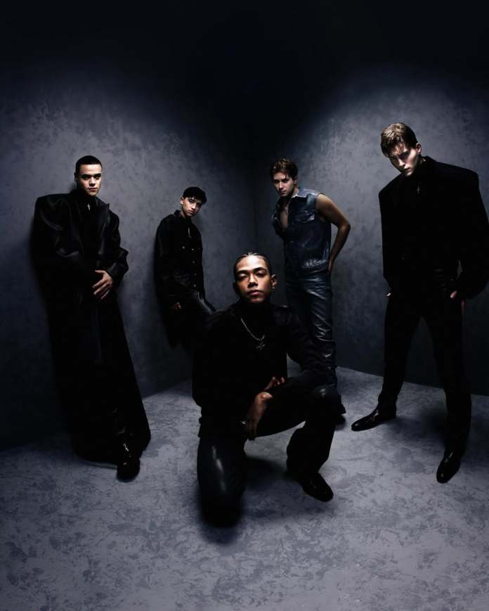 SANTOS BRAVOS members posing together in a dramatic and moody setting, wearing stylish black and denim outfits, with one member crouching in the foreground.