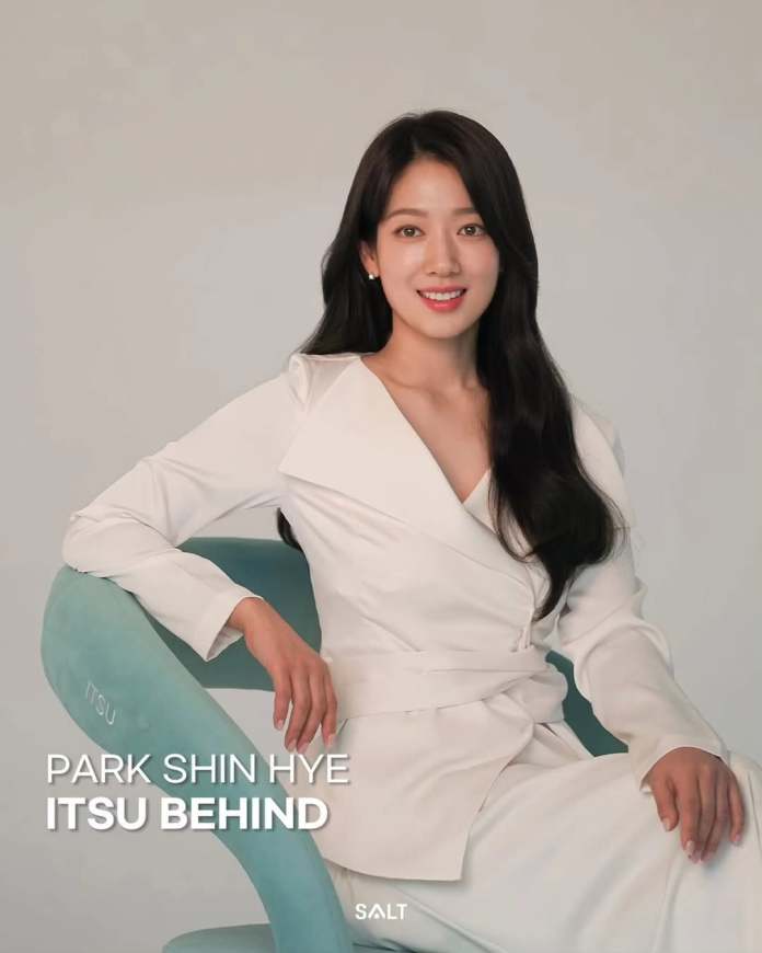 Park Shin-hye in a white outfit sitting on a teal chair, smiling at the camera with a neutral background.