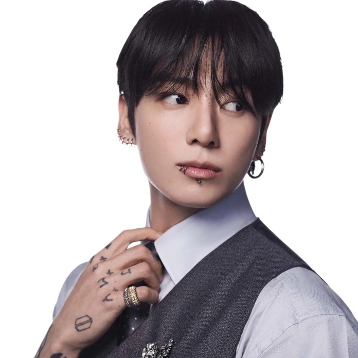 Jungkook with dark hair, styled slightly messy, wearing a formal outfit with a vest and a white shirt. He has multiple earrings and visible tattoos on his hands. The background is plain white, emphasizing his pose as he looks to the side.