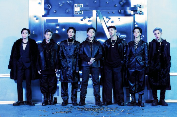 BTS dressed in black outfits striking a pose in front of a metallic backdrop with blue lighting.