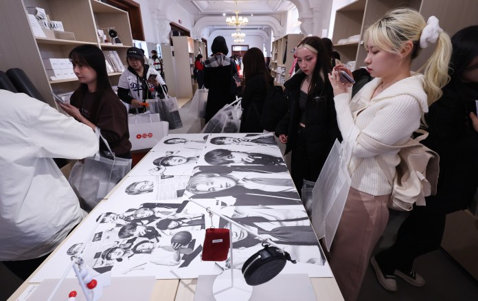A group of people shopping in a trendy store, with several individuals examining merchandise on a table covered with black-and-white photos. Some shoppers are holding shopping bags and using their phones.