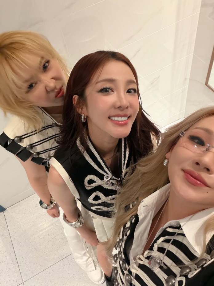 Sandara Park, CL and Minzy posing for a selfie, smiling and wearing stylish outfits with a black and white color scheme.