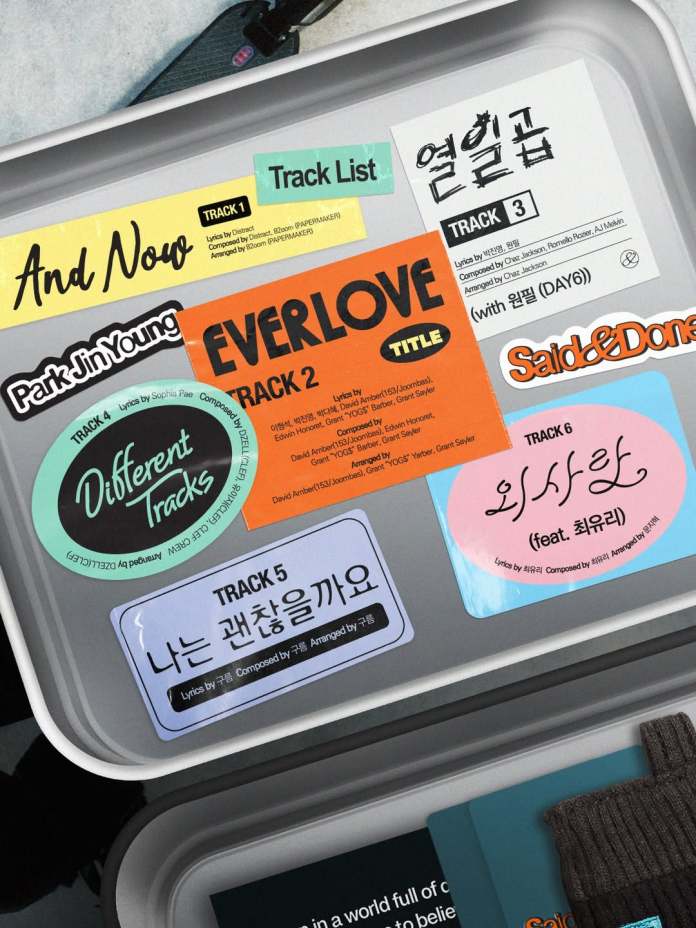 A collection of colorful tracklist stickers from an album, featuring titles and credits for multiple songs, displayed on a gray surface.