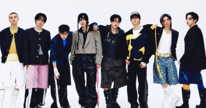 Stray Kids members posing together in fashionable outfits, featuring a mix of styles including oversized jackets, colorful shirts, and unique bottoms like shorts and skirts, against a plain white background.