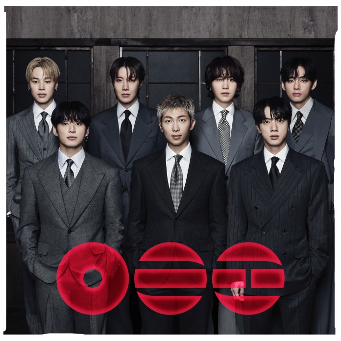 BTS members standing together, all dressed in stylish suits, with a dark, modern background.