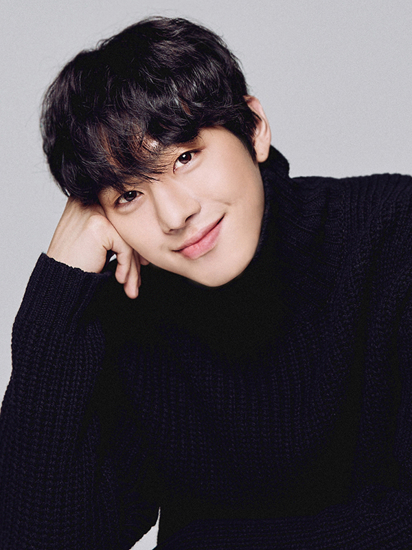 Smiling Ahn Hyo-seop with tousled dark hair resting his chin on his hand, wearing a black turtleneck sweater against a soft gray background.