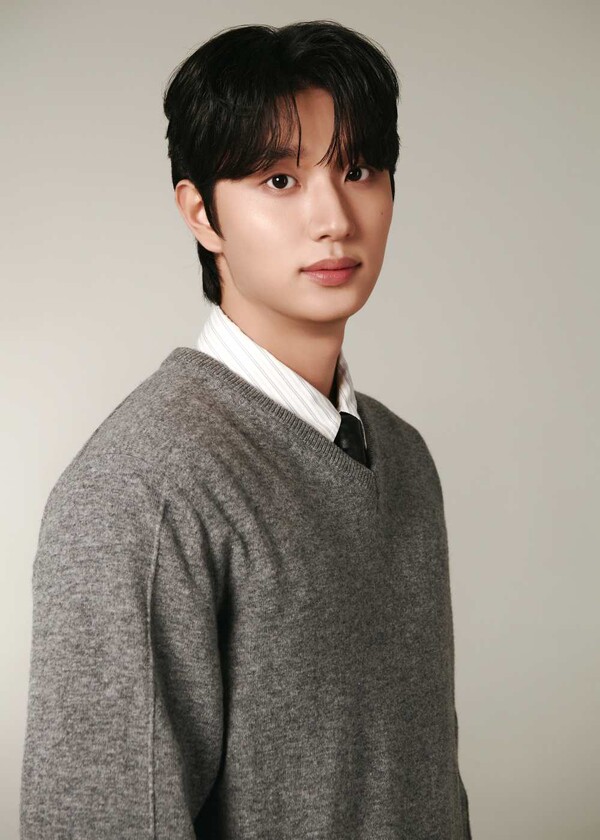 Kim Jaewon with dark hair wearing a gray sweater over a white collared shirt and a black tie, posing against a light background.