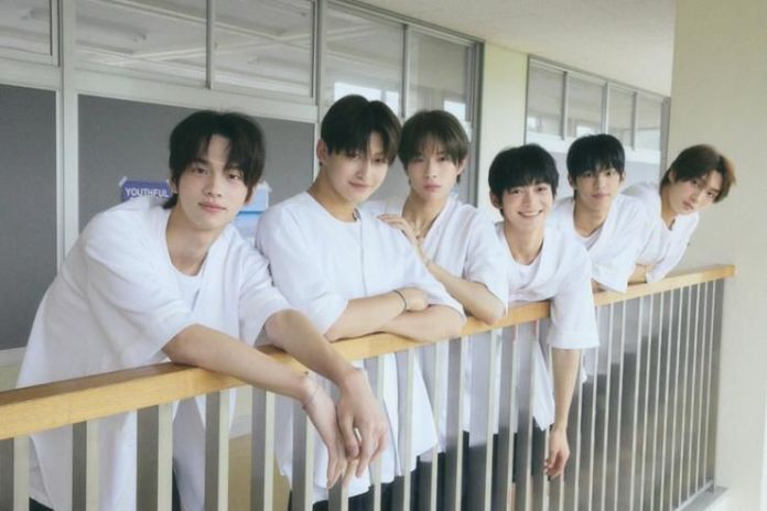 TWS in white shirts standing together on a balcony, smiling and posing for the camera.