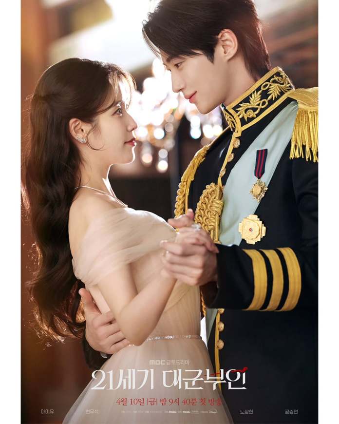 A romantic scene featuring Byeon Woo-seok in an elaborate military uniform and IU in a flowing gown, gazing into each other's eyes as they dance, with a softly lit background.