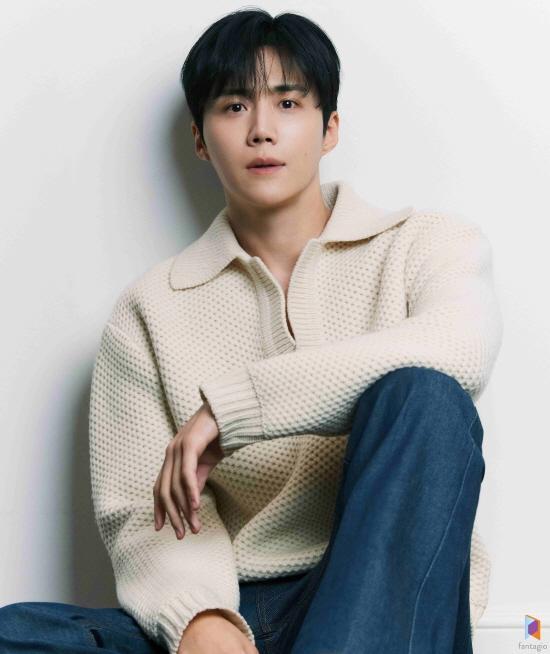 Kim Seon-ho in a light beige knit sweater with a collar, sitting on the floor and looking at the camera, styled with dark hair and wearing blue jeans.