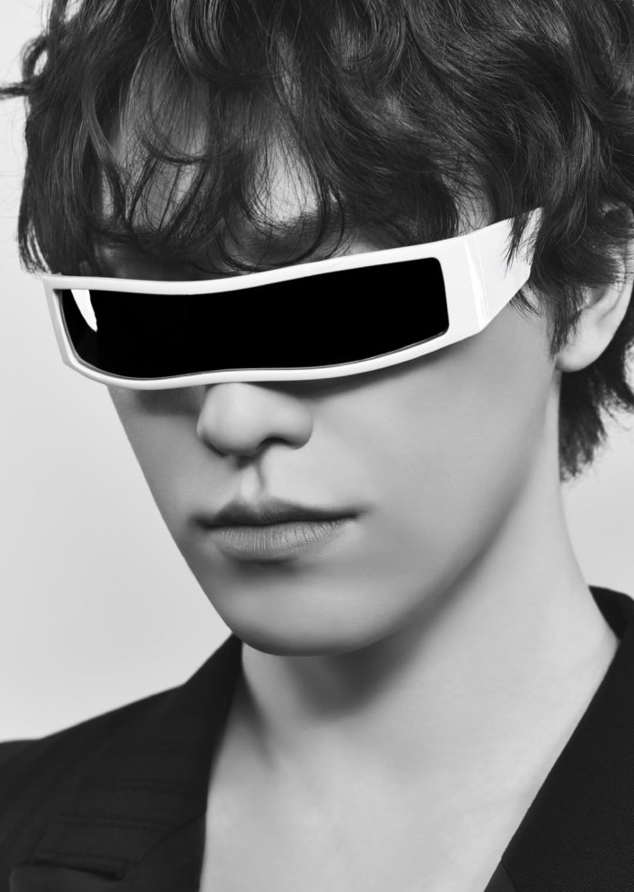 Close-up portrait of Dino with curly hair wearing futuristic white sunglasses, against a plain background.