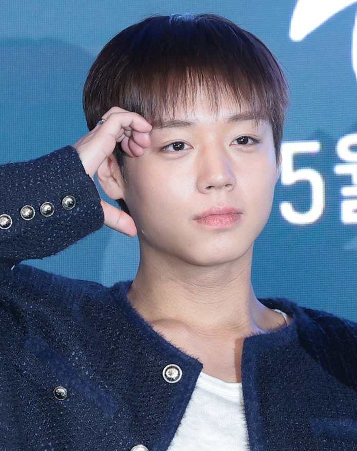 Park Ji-hoon wearing a dark jacket with decorative buttons, posing thoughtfully with one hand near his forehead and a serious expression.