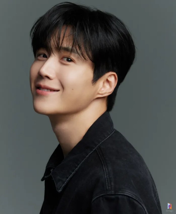 Kim Seon-ho with black hair smiles gently while facing to the left, wearing a dark jacket against a muted gray background.