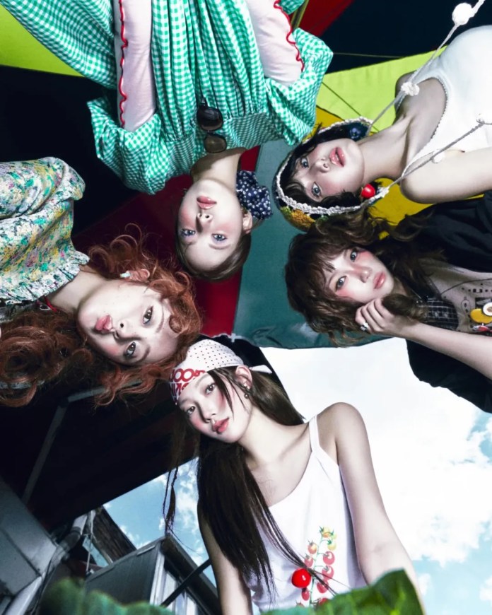 LESSERAFIM members posing together from a low angle, wearing colorful outfits and accessories, set against a vibrant backdrop of bright canopies and a clear sky.