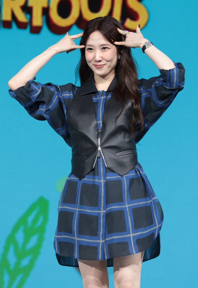 Park Eun-bin in a black and blue patterned dress playfully gestures with her fingers by her temples while smiling at the camera. She has long, dark hair and is standing in front of a colorful background.
