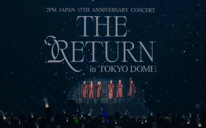 2PM standing on stage during a concert titled 'THE RETURN' in Tokyo Dome, celebrating 2PM's 15th anniversary, with a festive backdrop and audience illuminated by light sticks.