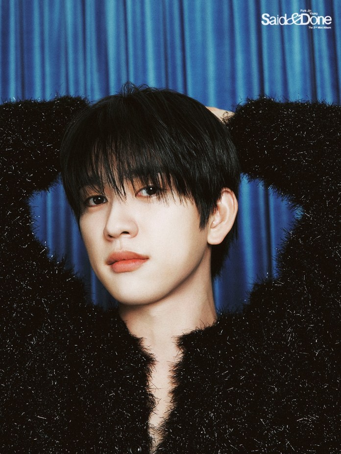 A close-up portrait of Park Jinyoung with dark hair styled to one side, wearing a fuzzy black sweater, against a blue curtain background.