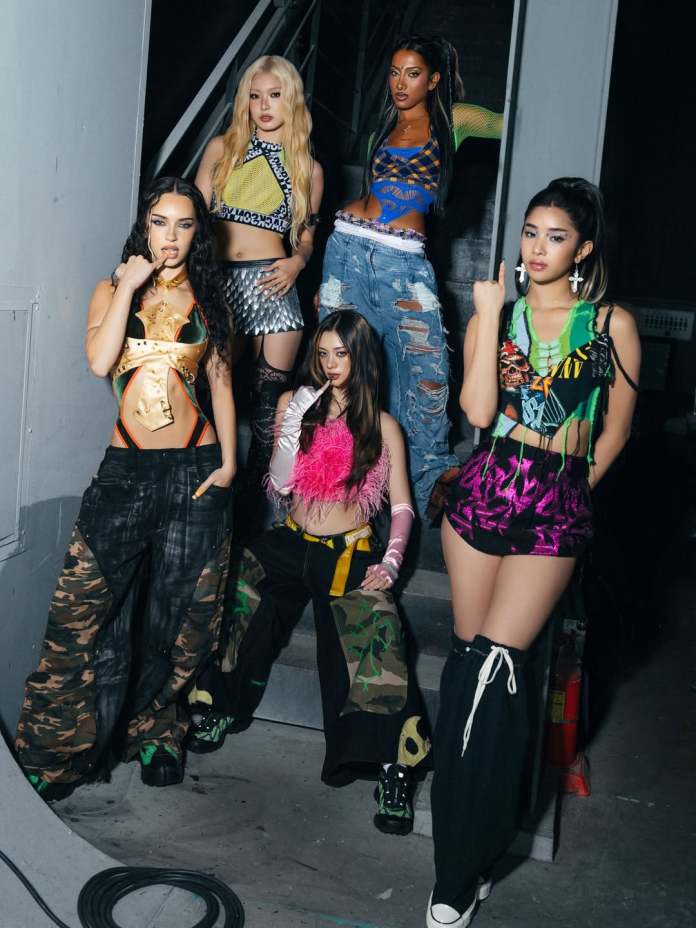 Katseye members posing together on a staircase, dressed in colorful and edgy fashion outfits, showcasing a mix of textures and styles.