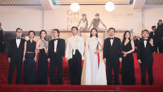 Jun Ji-hyun, Koo Kyo-hwan, Ji Chang-wook, Shin Hyun-bin, and Kim Shin-rock elegantly dressed individuals, including men in tuxedos and women in formal gowns, pose on the red carpet at the Cannes Film Festival, with a backdrop featuring the festival's logo.