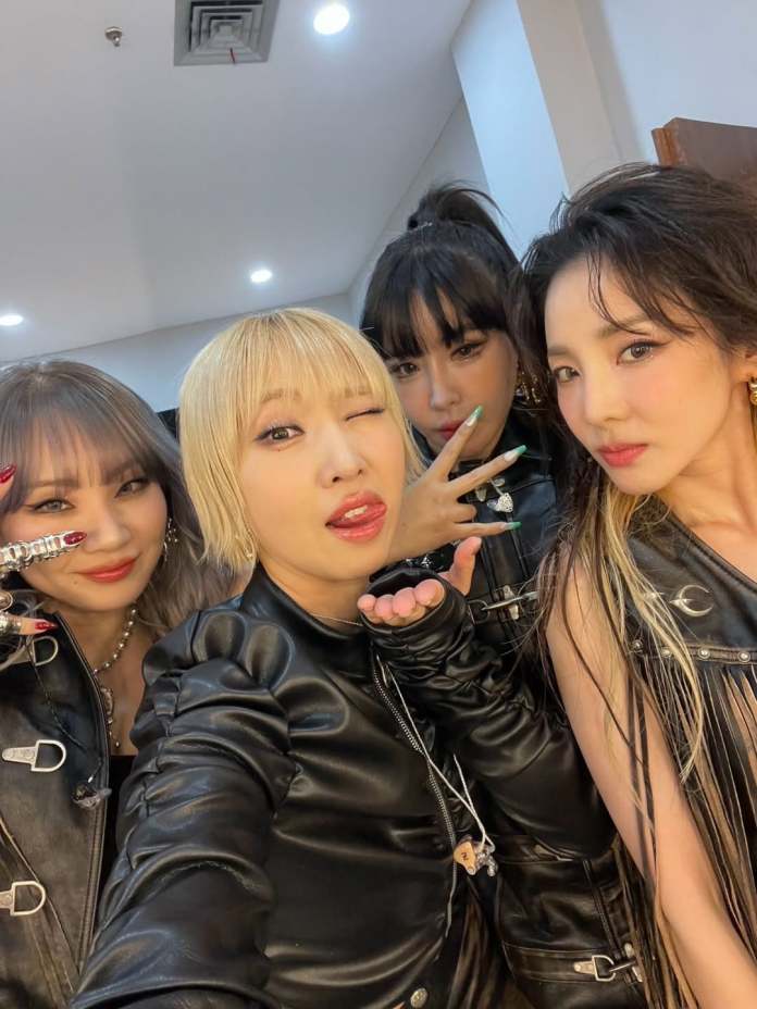 2ne1 members in leather outfits posing for a selfie, with playful expressions and stylish hairstyles, in a well-lit room.