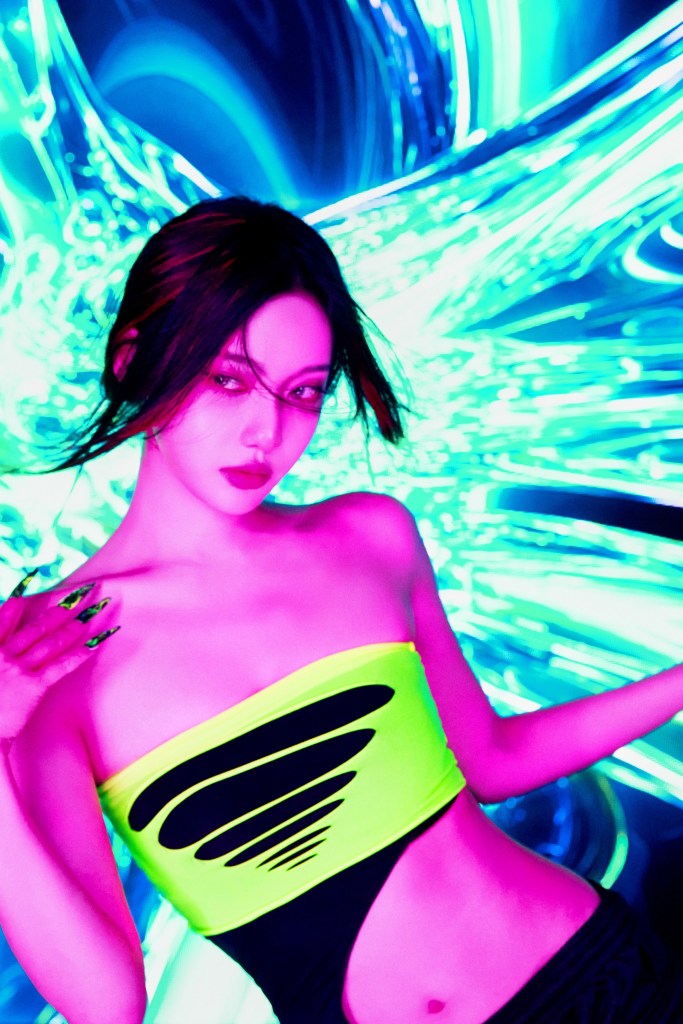 A person with long dark hair poses confidently in a vibrant neon green and black outfit against a colorful, swirling light background.
