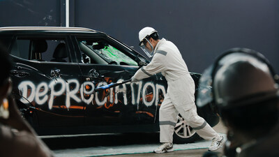 A participant in protective gear smashes a decommissioned car labeled with the financial burdens related to car ownership.