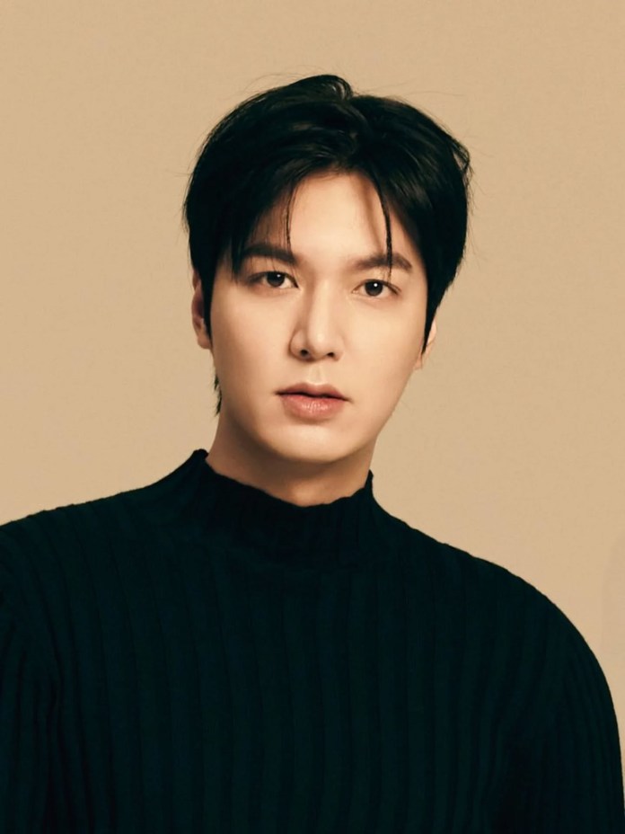 Lee Min-ho with dark hair wearing a black ribbed sweater against a light beige background.
