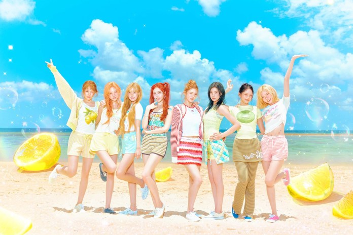 Hearts2Hearts posing on a beach with a vibrant blue sky and fluffy clouds. They are dressed in colorful summer outfits, surrounded by large lemon slices and sparkling bubbles, conveying a fun and cheerful atmosphere.