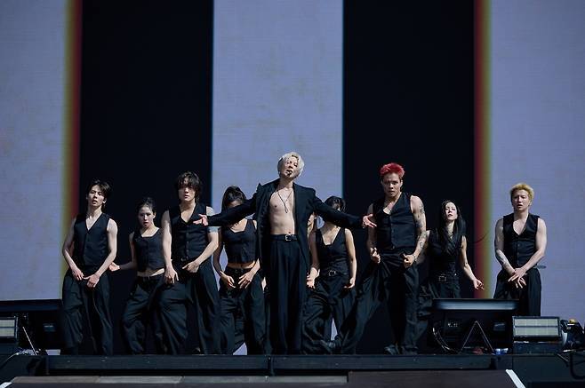 A group of performers in black outfits dancing on stage, with one central figure in a revealing top, showcasing a dynamic performance.